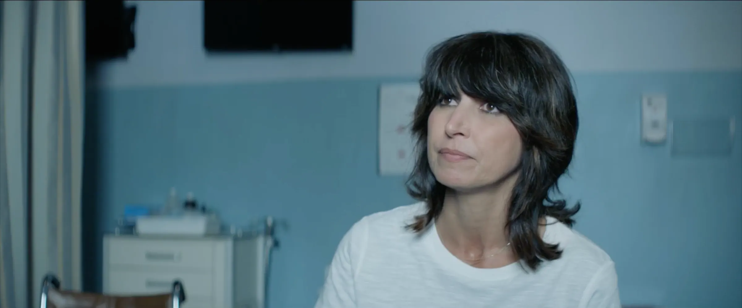 A woman stands in a pale blue hospital room.