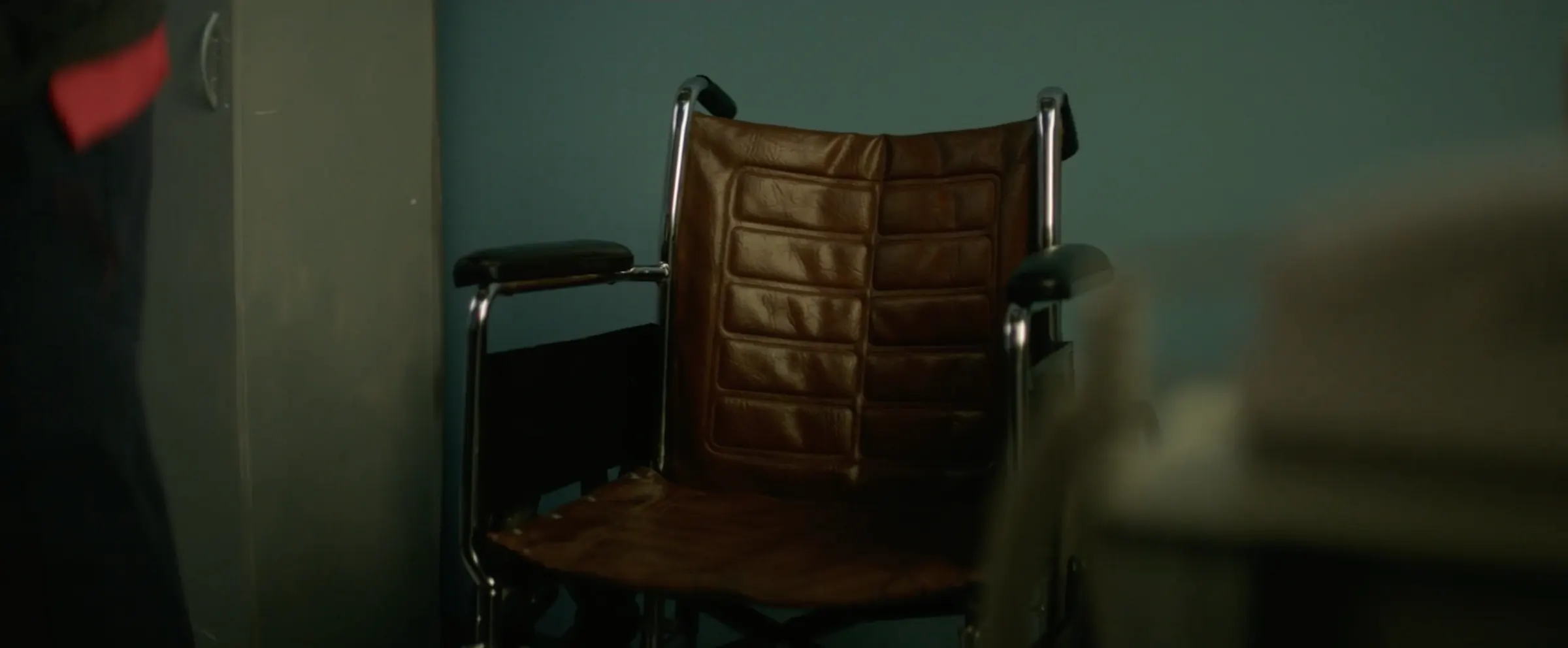 An empty wheelchair waits in a dim room.
