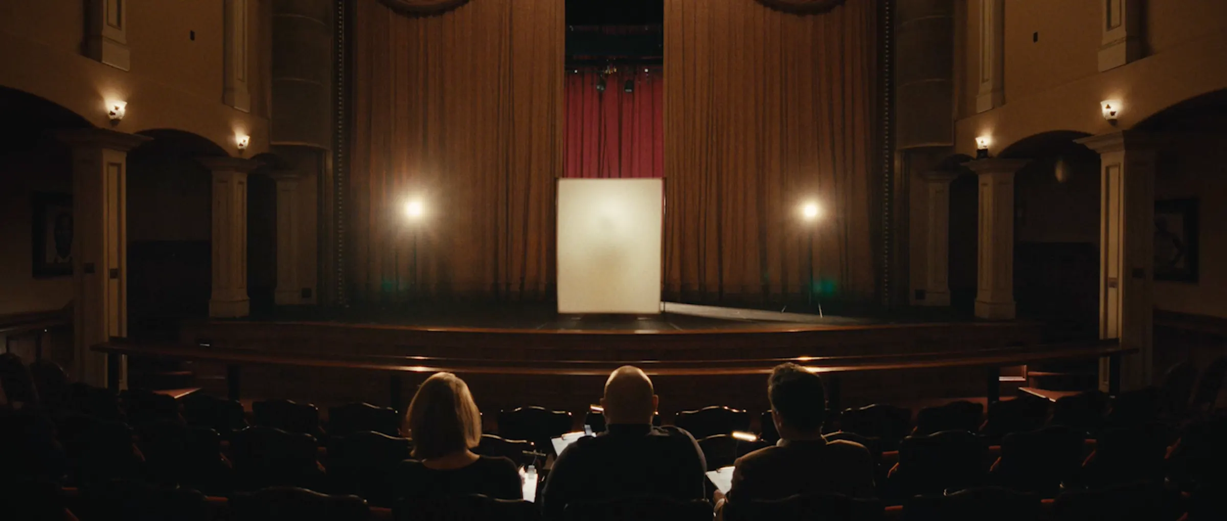 An audience waits in a darkened concert hall.
