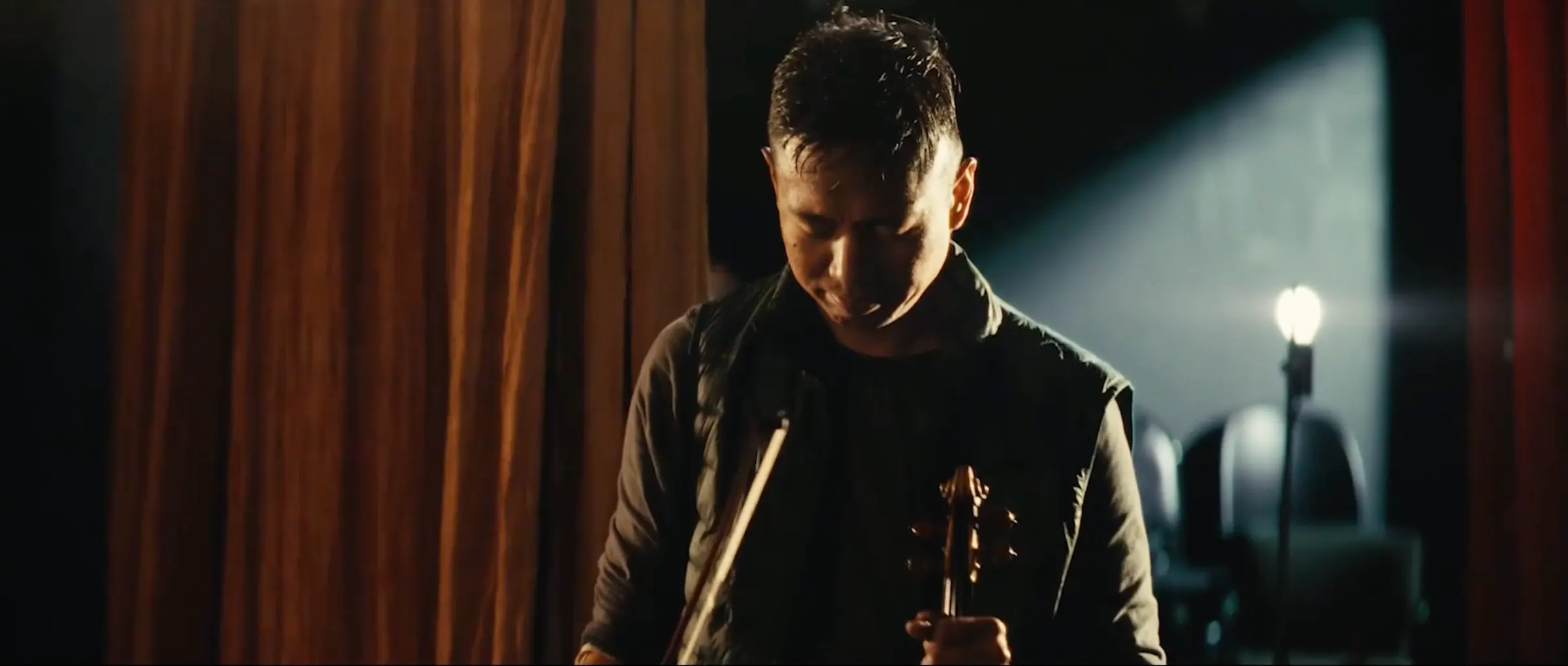 A violinist stands in a shaft of stage light.