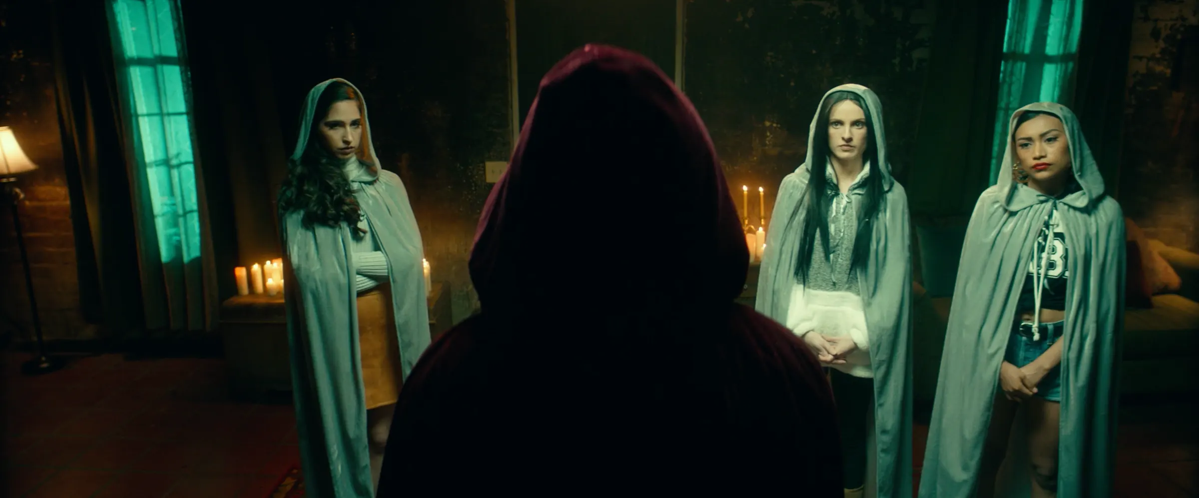 Hooded sisters flank a pledge in a candlelit room.
