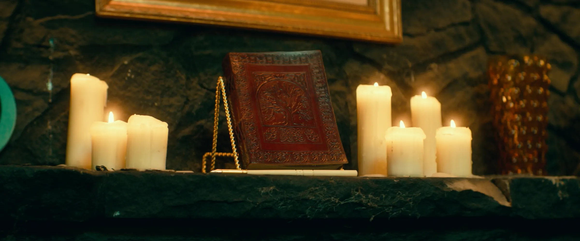 Candles and a red spellbook on a mantel.