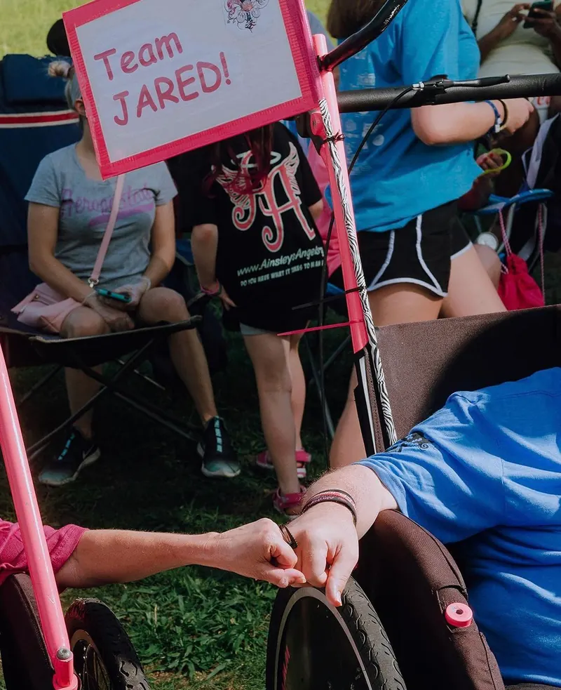 Supporters hold a “Team Jared” sign beside a racing chair.